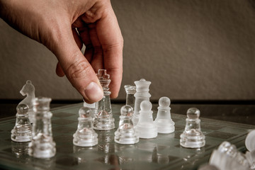 Hand moving the queen on the glass chessboard