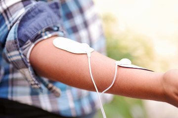 Close-up of a woman holding an electrode machine in her hand and with electrostimulator electrodes in the arm in a blurred background