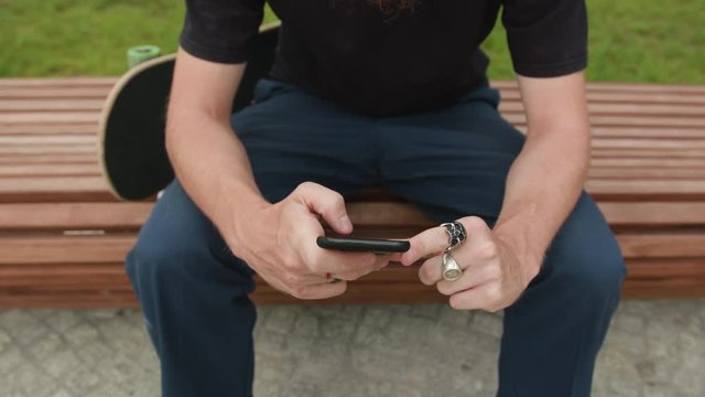Young readhead hispter with beard and moustaches in jeans and T-shirt writes on smartfone. Outdoor. Cloudy. Close up