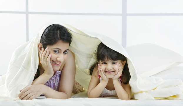 Portrait of mother and daughter under a bed sheet 