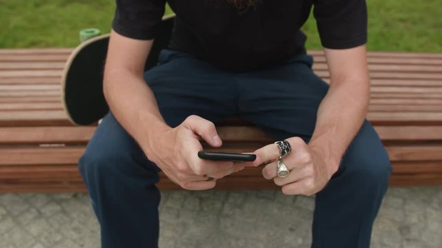 Young readhead hispter with beard and moustaches in jeans and T-shirt writes on smartfone. Outdoor. Cloudy. Stabilised. Close up