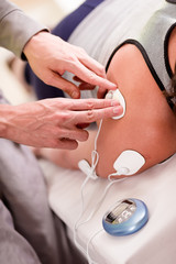 Naklejka premium Close-up of a personal trainer hand putting an electrostimulator electrodes in the shoulder of a female deportist, upside down on a bed