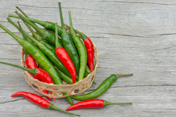 Fresh chili peppers, red and green are in the little basket woven from bamboo. Placed on the wooden floor.