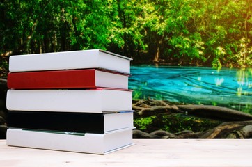 stack book on desk, no labels, blank spine with blurred view of amazing beautiful emerald pool and blue pool in forest with sunlight effect, education back to school, landscape nature, copy space