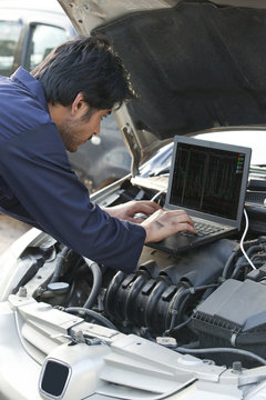 Mechanic using laptop while repairing car engine