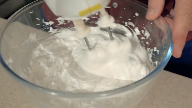 Closeup of a man pounding a mixer cream in a transparent bowl