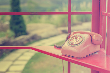 Old retro red phone in red phone booth with natural green view.