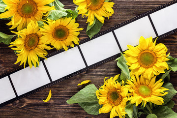 Background with frame in the form of a film and bright sunflowers on dark wooden table.