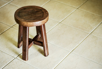 Solid low wooden stool on light color tile floor. Art studio round stool.