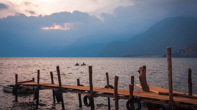 Boardwalk over Lake Atitlan on the shore of Panajachel village in Guatemala at sunset with some kayakers in mid-ground.
