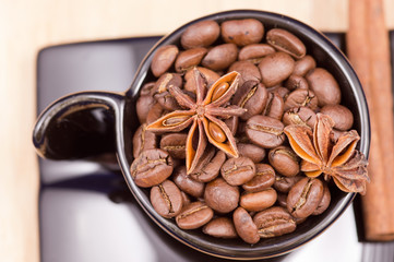 Black cup filled with coffee beans, anise and cinnamon on wooden surface