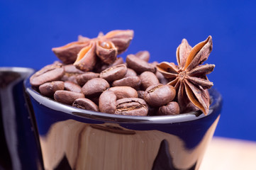 Black cup filled with coffee beans, anise and cinnamon on wooden surface