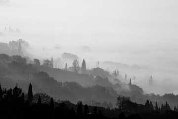 Fototapeta premium Fog and smoke covering a valley, with different layers of trees and some houses
