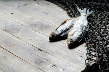 Dried and salty fish and fishing nets on the wooden background. Still-life and objects.