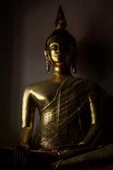 A statue of Gold Buddha with shadow on wall in the dark room