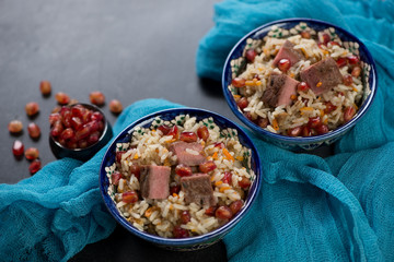 Pilaf with beef meat and pomegranate seeds served in two bowls, closeup, horizontal shot