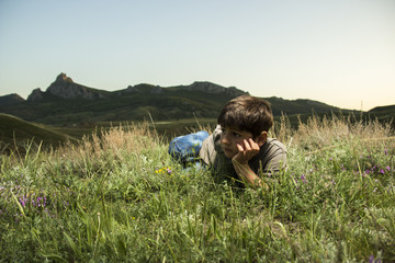 Fototapeta na wymiar Boy lying in grass at backdrop of the mountains