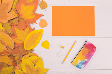 Empty orange paper and school supplies on wooden table with painted leaves.