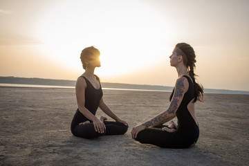Two young fit womans meditating in lotus during the sunset 