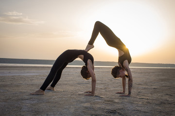 young women practicing yoga poses and asanas. Partner yoga, acrobatic yoga. Yoga class in black wear training in desert during sunset