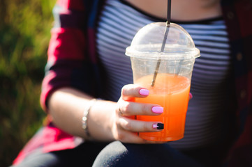 Beautiful girl with an orange cocktail on the grass in the park