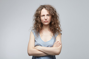Indoor shot of angry attractive grumpy young female dressed casually keeping arms folded, looking...