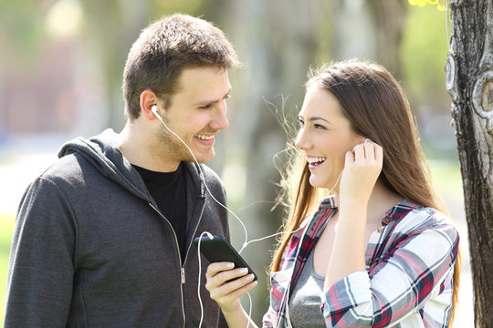 Happy couple of teens sharing music outdoors