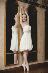Young ballerina with a perfect body is dancing in the dance hall. Beautiful girl standing near mirrors