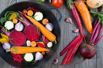 Raw sliced vegetables for roasting, on a baking tray. Assortment of vegetables from the garden. Healthy food .Carrot, beet, chard, zucchini, onion, garlic, tomato.