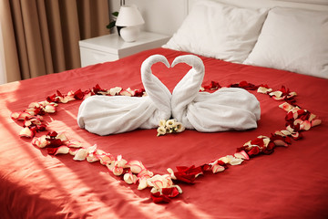 Two towel swans and rose petals on bed in hotel room © Africa Studio