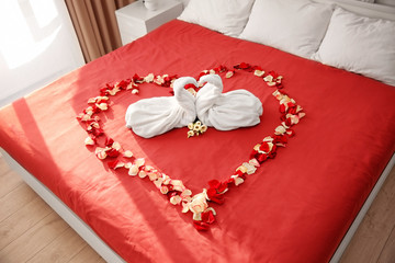 Two towel swans and rose petals on bed in hotel room