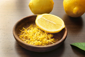 Bowl with fresh zest and half of lemon on wooden table