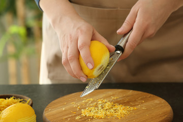 Woman grating zest of lemon on kitchen table