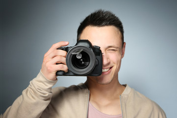 Handsome photographer with camera on gray background