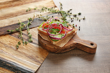 Wooden board with delicious toast and vegetables on table