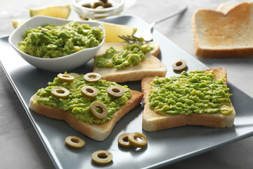 Bowl and delicious toasts with avocado and olives on platter