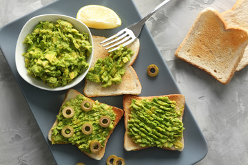 Bowl and delicious toasts with avocado and olives in platter on stone table