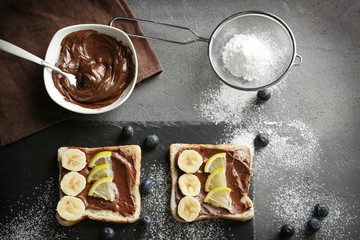 Delicious toasts with banana, chocolate spread and lemon on dark table