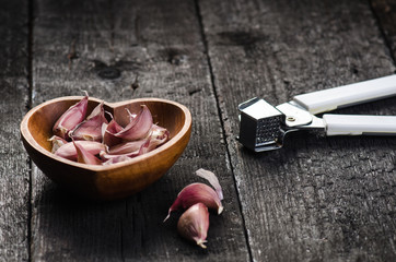 Cloves of garlic on a wooden black table. Fresh garlic bulb with iron garlic press. Vintage background.  Farmer. Medicine and healthy. Traditional medicine. bowl shape of heart