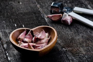 Cloves of garlic on a wooden black table. Fresh garlic bulb with iron garlic press. Vintage background.  Farmer. Medicine and healthy. Traditional medicine. bowl shape of heart