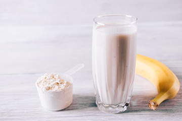 Protein cocktail in a glass, scoop and banana on a white wooden table