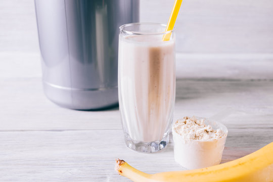 Banana, protein shake in a glass and scoop on white wooden table