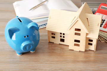 Piggy bank, stationery and house model on table. Savings concept