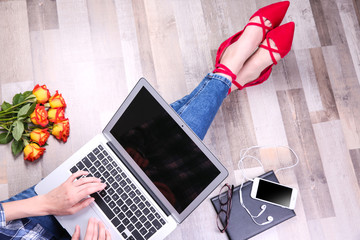 Young woman in stylish flat shoes with laptop sitting on floor