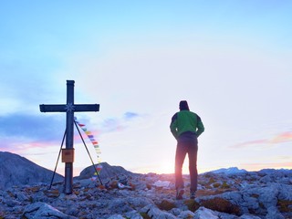 Tourist stand on rocky view point and watching into misty Alpine valley. Wooden cross