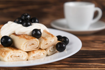 Breakfast. Pancakes on a wooden table with cheese and black currants. In the background a Cup of coffee.