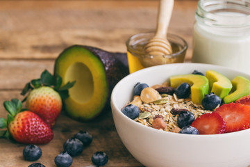 Muesli or granola on white bowl with fresh fruits nuts and cereal. Granola top with blueberries strawberries and avocado served with milk and honey for breakfast.Granola is healthy food for dieting.