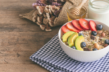 Muesli or granola on white bowl with fresh fruits nuts and cereal. Granola top with blueberries strawberries and avocado served with milk and honey for breakfast.Granola is healthy food for dieting.
