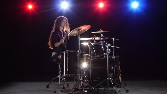 Girl drummer with chopsticks beats rhythmic music. Black background . Red light blue. Side view