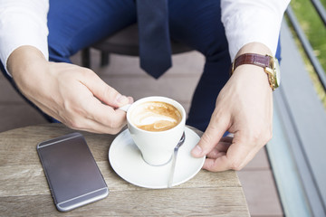 Close up of business man hands with cup of coffee and phone